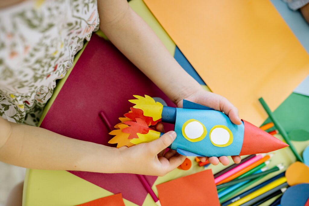 A child builds a vibrant paper rocket during an arts and crafts session, fostering creativity.